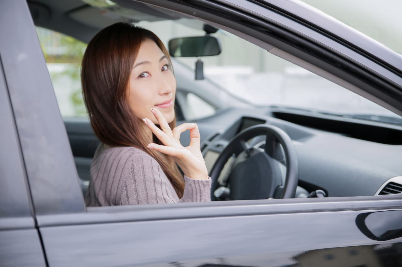 車の運転席からグッドマークをしている女性